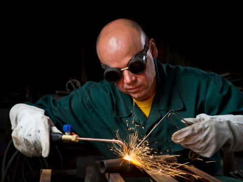 Worker oxy-fuel welding a metal pipe with sparks flying